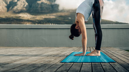 Frau übt Yoga-Positionen auf der Terrasse ihres Hauses. Fitness-Frau in einer Yoga-Haltung, die sich nach unten beugt, wobei die Handflächen den Boden berühren. - JLPSF27004