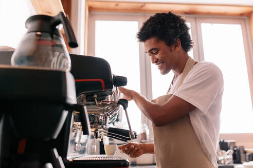 Professioneller Barista hält Tasse auf der Kaffeemaschine. Junger Mann macht Kaffee mit einer Espressomaschine im Café. - JLPSF27014