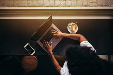 Draufsicht auf einen jungen Mann, der in einem Café sitzt und am Laptop arbeitet. Aufnahme von oben eines Mannes, der in einem Café am Laptop arbeitet - JLPSF27047