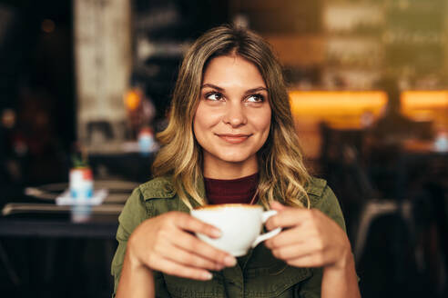 Porträt einer schönen jungen Frau, die mit einer Tasse Kaffee im Café sitzt und wegschaut. Kaukasische Frau trinkt Kaffee im Café - JLPSF27051