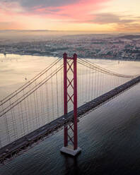 Luftaufnahme der Brücke vom 25. April über den Tejo bei Sonnenuntergang mit der Innenstadt von Lissabon im Hintergrund, Lissabon, Portugal. - AAEF16604