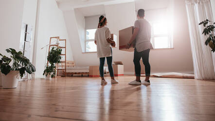 Rückansicht in voller Länge eines jungen Paares, das Kartons in ein neues Haus trägt. Junger Mann und Frau halten Kartons und ziehen in ein neues Haus. - JLPSF27059