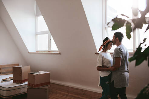Indoor shot of loving young couple moving into their new home. Man and woman in love standing together with cardboard boxes in room. - JLPSF27062