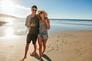 Außenaufnahme eines romantischen jungen Paares, das am Strand spazieren geht. Junger Mann und Frau, die an einem Sommertag am Meer spazieren gehen und lächeln. - JLPSF27070