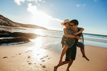 Romantic young couple enjoying summer holidays. Handsome young man giving piggyback ride to girlfriend on beach. - JLPSF27075