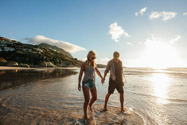 Outdoor shot of happy young couple walking on the beach holding hands. Young man and woman enjoying beach holidays. - JLPSF27078