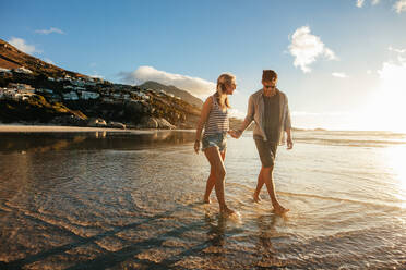 Full length shot of young couple holding hands walking on the beach. Young man and woman strolling on the sea shore. - JLPSF27079