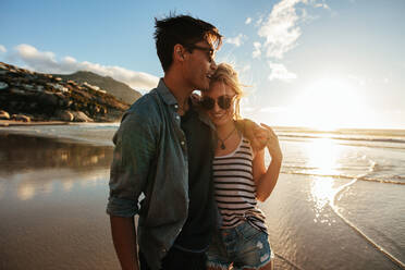 Outdoor shot of romantic young couple standing together on beach. Young man and woman on seashore at sunset. - JLPSF27084