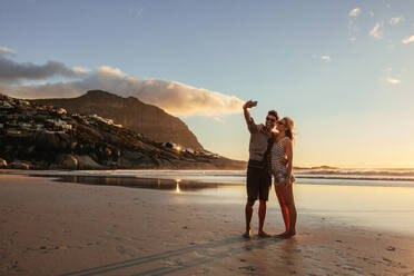 Romantisches junges Paar macht Selfie mit Handy am Strand. Mann und Frau am Meer machen Selfie bei Sonnenuntergang. - JLPSF27090
