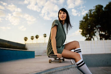 Schöne Skateboarderin auf dem Skateboard sitzend. Urbanes Mädchen entspannt sich im Skatepark. - JLPSF27103