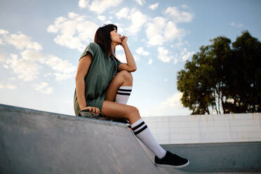 Frau sitzt auf der Skaterrampe, schaut weg und denkt an den Skatepark. Junge Frau auf dem Skateboard entspannt im Skatepark. - JLPSF27105