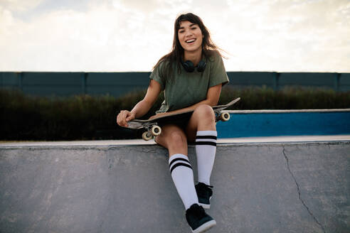 Attraktive Frau sitzt auf der Rampe im Skatepark. Urbanes Mädchen mit Skateboard entspannt sich und verbringt Zeit im Skatepark. - JLPSF27112