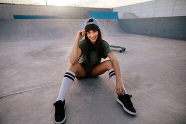 Porträt eines attraktiven urbanen Mädchens, das entspannt im Skatepark sitzt. Eine Skateboarderin macht eine Pause nach dem Skateboarding im Freien. - JLPSF27119