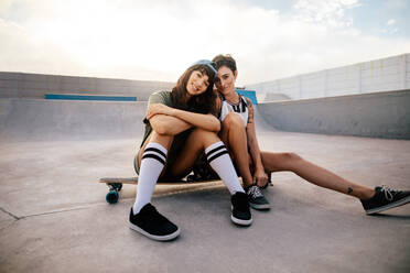 Zwei weibliche Skateboarderinnen sitzen auf einem Longboard im Skatepark. Freundinnen hängen zusammen im Freien im Skatepark ab. - JLPSF27123