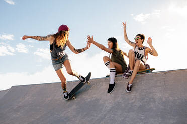 Weibliche Skateboarderin fährt Skateboard im Skatepark mit Freunden, die auf der Rampe sitzen und Spaß haben. - JLPSF27142