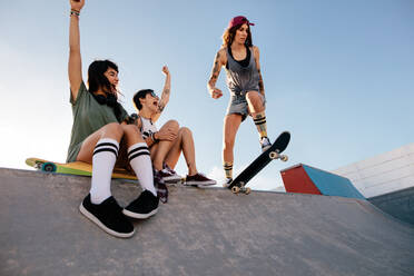 Drei junge Freundinnen im Skatepark: Skaterin beginnt ihr Programm, während ihre Freundinnen auf der Rampe sitzen und sie anfeuern. - JLPSF27145