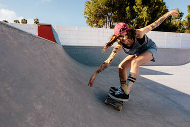 Skater female rides on skateboard at skate park ramp. Young woman practising skateboarding outdoors at skate park. - JLPSF27150