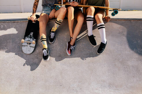Beine von Frauen, die auf einer Rampe im Skatepark sitzen. Ausgeschnittene Aufnahme von Skaterinnen, die sich nach dem Skateboarding auf der Rampe ausruhen. - JLPSF27165