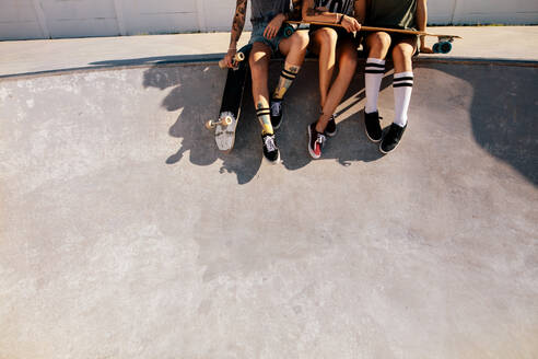 Ausschnitt von drei Frauen, die nach dem Skateboardfahren auf einer Rampe sitzen. Beine von Skaterinnen, die im Skatepark zusammensitzen. - JLPSF27166