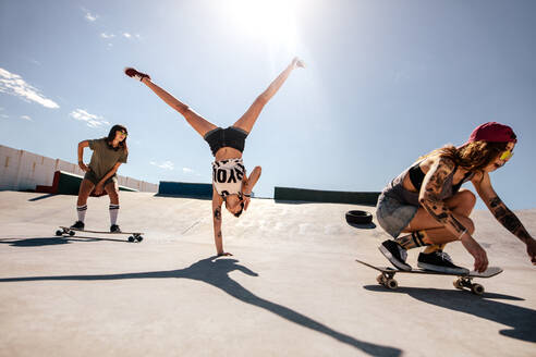 Frau macht Flip mit Freundinnen Skateboarding im Skatepark. Gruppe von Frauen genießen im Skatepark. - JLPSF27184