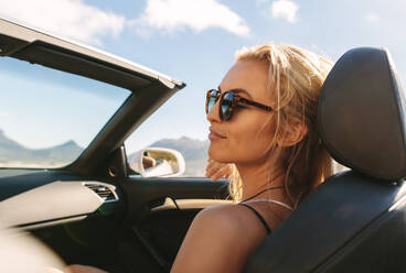 Kaukasische Frau mit Sonnenbrille, die entspannt auf dem Beifahrersitz eines Cabriolets sitzt. - JLPSF27185