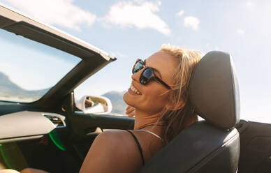 Attraktive junge Frau sitzt auf dem Beifahrersitz eines Autos und lächelt. Frau reist mit einem Cabrio auf Road Trip. - JLPSF27186