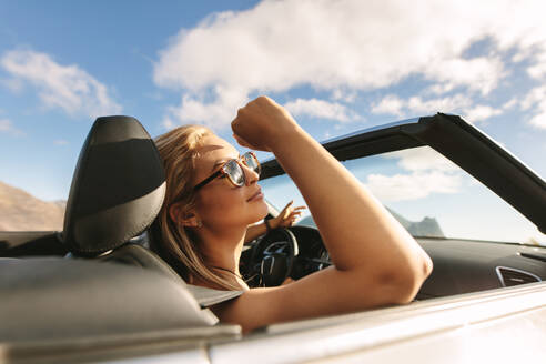 Attraktive Frau mit Sonnenbrille, die in einem Cabrio reist. Frau auf einer Autoreise, die im Auto fährt. - JLPSF27200