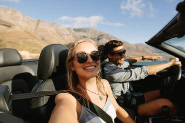 Beautiful woman talking selfies with her boyfriend driving a car. Couple talking selfies on road trip. - JLPSF27201