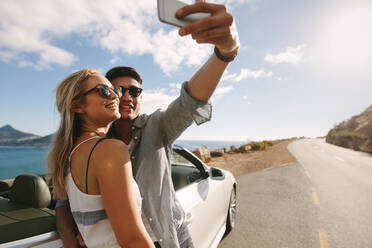 Attraktiver Mann und Frau mit Sonnenbrille nehmen Selfie-Foto zusammen, während stehend von Auto auf der Autobahn. - JLPSF27212