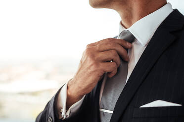 Nahaufnahme eines Mannes im Geschäftsanzug, der seine Krawatte zurechtrückt. Ausschnitt eines Geschäftsmannes, der seinen Look zurechtrückt. - JLPSF27216
