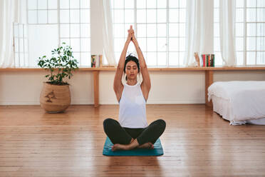 Volle Länge Schuss von gesunden und schönen jungen Frau sitzt zu Hause in Yoga-Position. Fitness weiblichen sitzen mit den Händen über ihrem Kopf verbunden. - JLPSF27223