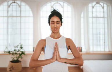 Portrait of healthy young woman standing at home with her hands joined. Beautiful female meditating at home. - JLPSF27227