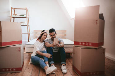 Young couple moving in new home and taking selfie. Young man and woman sitting on floor making selfie with smart phone. - JLPSF27236