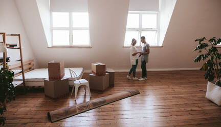 Young couple in love moving in a new apartment. Man and woman standing together with boxes and carpet on floor. - JLPSF27242