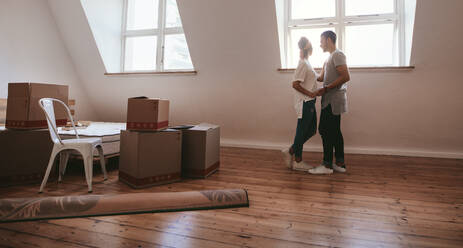 Junger Mann und verliebte Frau ziehen in eine neue Wohnung um. Junges Paar steht zusammen mit Kisten und Teppich auf dem Boden. - JLPSF27243