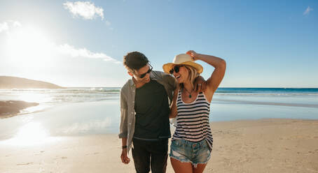 Horizontale Aufnahme eines glücklichen jungen Paares am Strand: Ein junger Mann und eine junge Frau gehen am Strand spazieren und lachen. - JLPSF27263