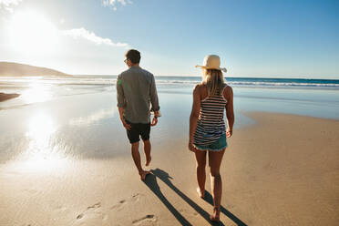 Rückansicht eines jungen Mannes und einer Frau, die am Meer spazieren gehen. Ein Paar im Sommerurlaub am Strand. - JLPSF27265