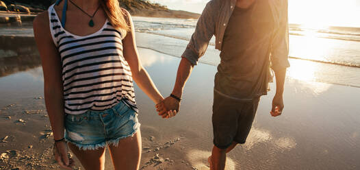 Ausschnitt eines jungen Mannes und einer Frau, die sich an den Händen halten und am Strand spazieren gehen. Paar, das am Meer spazieren geht. - JLPSF27274