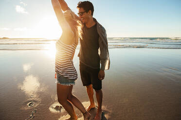 Aufnahme eines verliebten jungen Paares, das an einem Sommertag am Strand tanzt. Junger Mann und Frau tanzen am Meer. - JLPSF27275