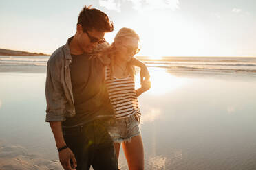 Außenaufnahme eines romantischen jungen Paares am Strand: Junger Mann und Frau gehen bei Sonnenuntergang am Meer spazieren. - JLPSF27288