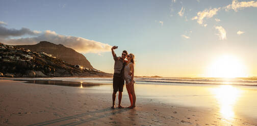 Horizontal shot of loving young couple taking self portrait at the beach. Man and woman on sea shore taking selfie with mobile phone. - JLPSF27295