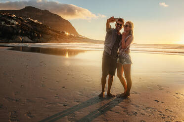 Romantisches junges Paar, das ein Selfie am Strand macht. Junger Mann und Frau am Meer, die bei Sonnenuntergang ein Selfie mit dem Handy machen. - JLPSF27297