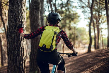 Rückenansicht eines Menschen mit Rucksack auf dem Fahrrad auf einem Weg zwischen Bäumen auf einem Hügel im Wald - ADSF39962