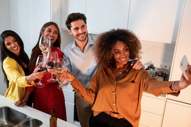 Glückliche junge gemischtrassige Freunde stoßen mit Wein an und machen ein Selfie mit ihrem Smartphone, während sie sich auf einer Party zu Hause amüsieren - ADSF40019