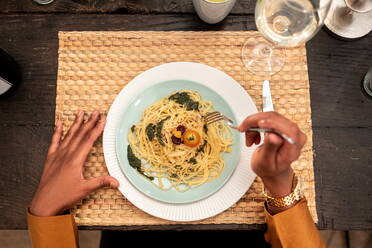 Top view of crop unrecognizable woman eating delicious homemade pasta while sitting at wooden table with snacks and drinks during dinner with friends - ADSF40022