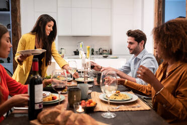 Eine Gruppe moderner junger multirassischer Freunde versammelt sich an einem festlichen Tisch mit köstlichen Gerichten und Wein und genießt die gemeinsame Zeit zu Hause - ADSF40027