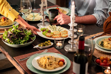 Crop friends gathering around festive table served with delicious homemade snacks and pasta with wine during home party - ADSF40028