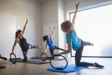 Weibliche Trainerin mit einer Gruppe von Frauen, die eine Übung mit einem Pilates-Ring machen, indem sie knien und ein Bein und einen Arm während des Trainings im Studio anheben - ADSF40103