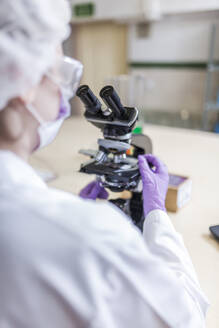 Back view of anonymous woman scientist looking through microscope at laboratory - ADSF40149