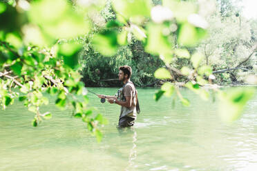 Side view of male fisherman throwing fishing rod into a mountain river - ADSF40153